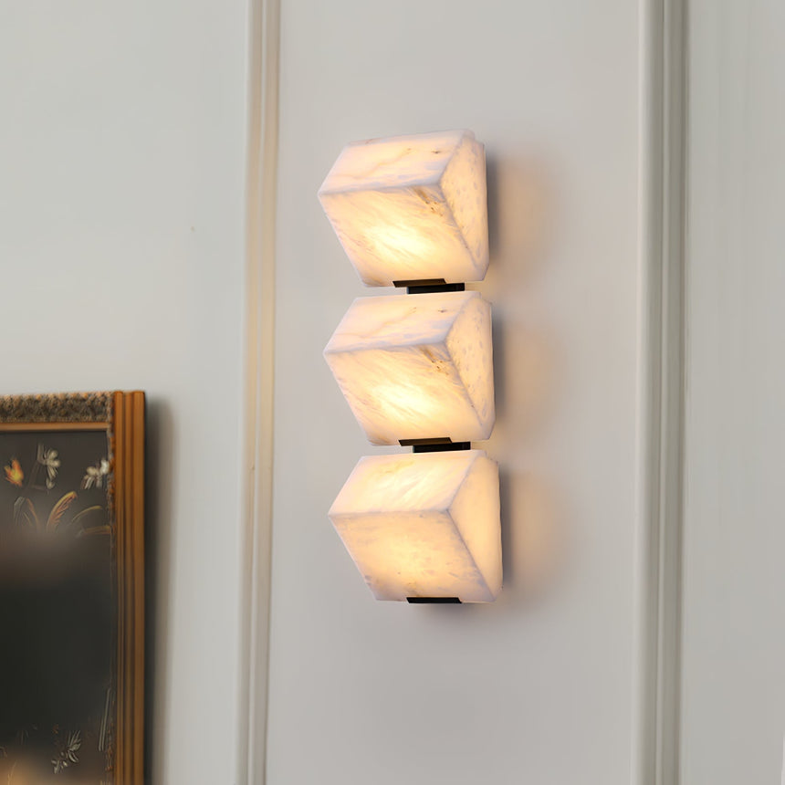 Stone three lit blocks on a paneled wall beside a gilt picture frame