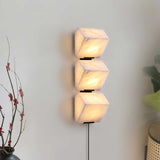 Three lit alabaster blocks on a pale wall beside a branch in a vase