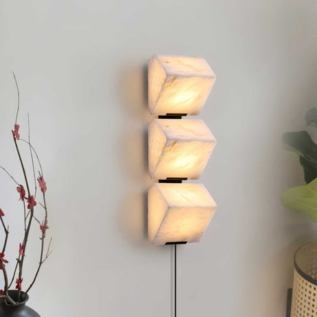 Three lit alabaster blocks on a pale wall beside a branch in a vase