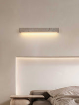 Travertine bar lit above a pale headboard beside a bedside table and a book