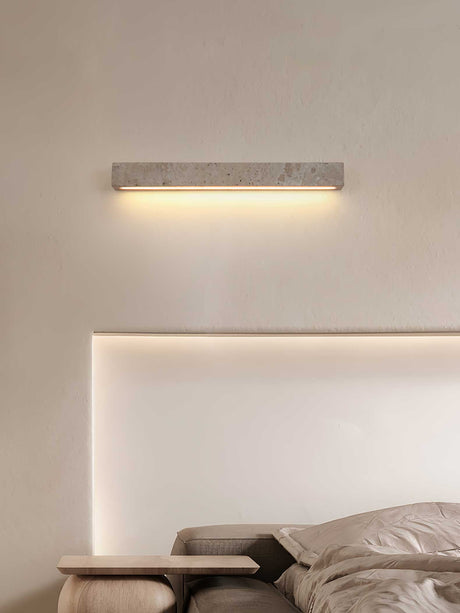 Travertine bar lit above a pale headboard beside a bedside table and a book