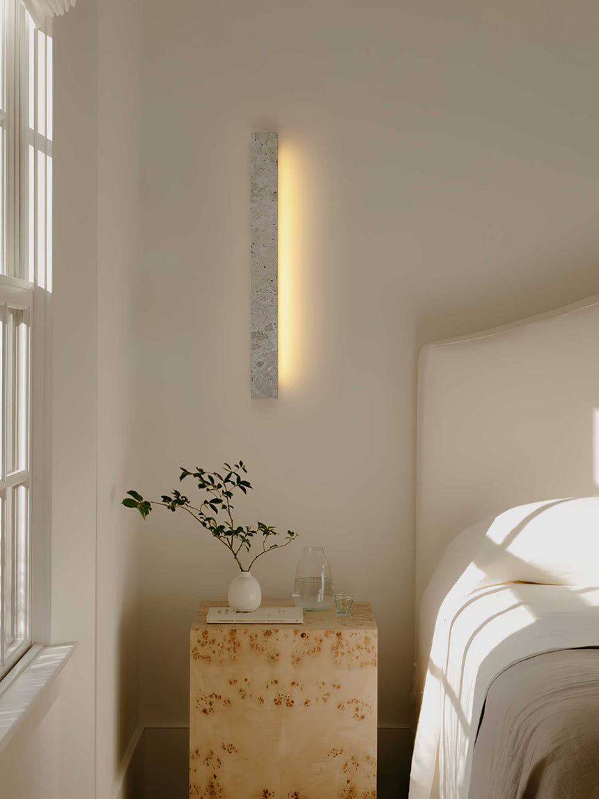 The bar mounted upright beside a bed, a tall warm line next to a stone nightstand