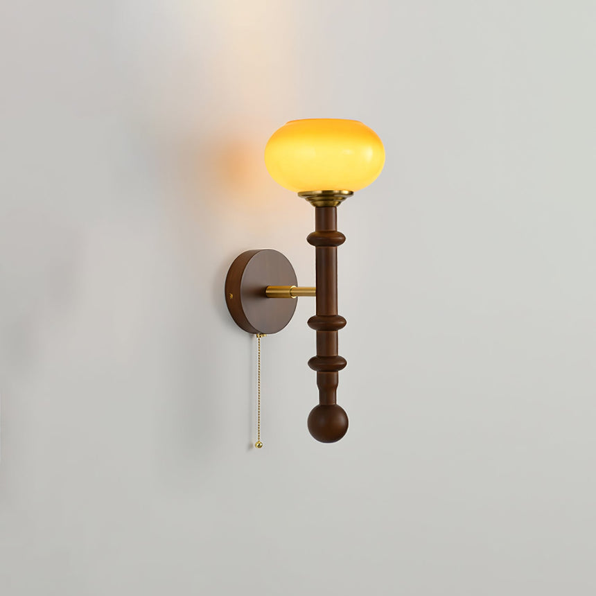 Amber glass shade lit warm at the top of a tall walnut column