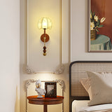 Walnut column sconce lit beside a bed above a round side table