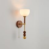 White bell shade lit, the walnut column and brass beads below it