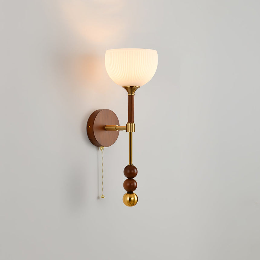 White bell shade lit, the walnut column and brass beads below it