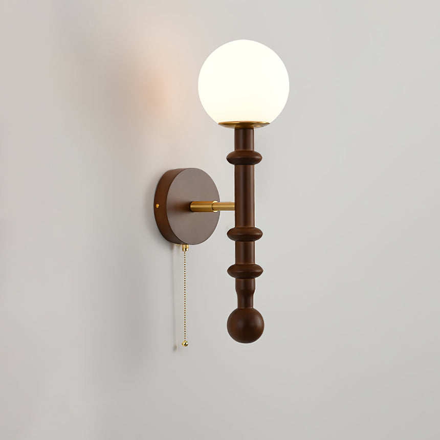 White globe lit warm above a slim walnut column and brass hardware