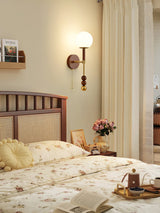 Walnut column sconce lit on a bedroom wall beside a spindle headboard