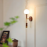 Walnut column sconce lit on a paneled wall above a chest of drawers