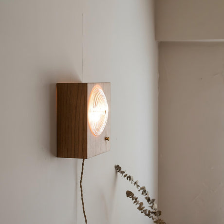 Wood box sconce lit and seen from an angle, the cord trailing to the floor