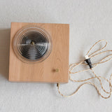 The wood box laid flat showing the ribbed lens and the braided fabric cord
