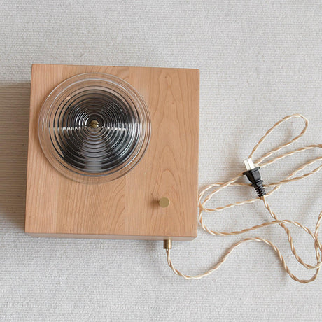 The wood box laid flat showing the ribbed lens and the braided fabric cord