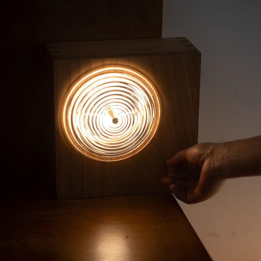 Ribbed glass lens glowing warm in a dark wood box against a dark wall