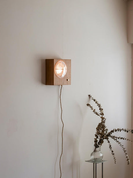 Wood box sconce lit on a wall above a small table with dried branches