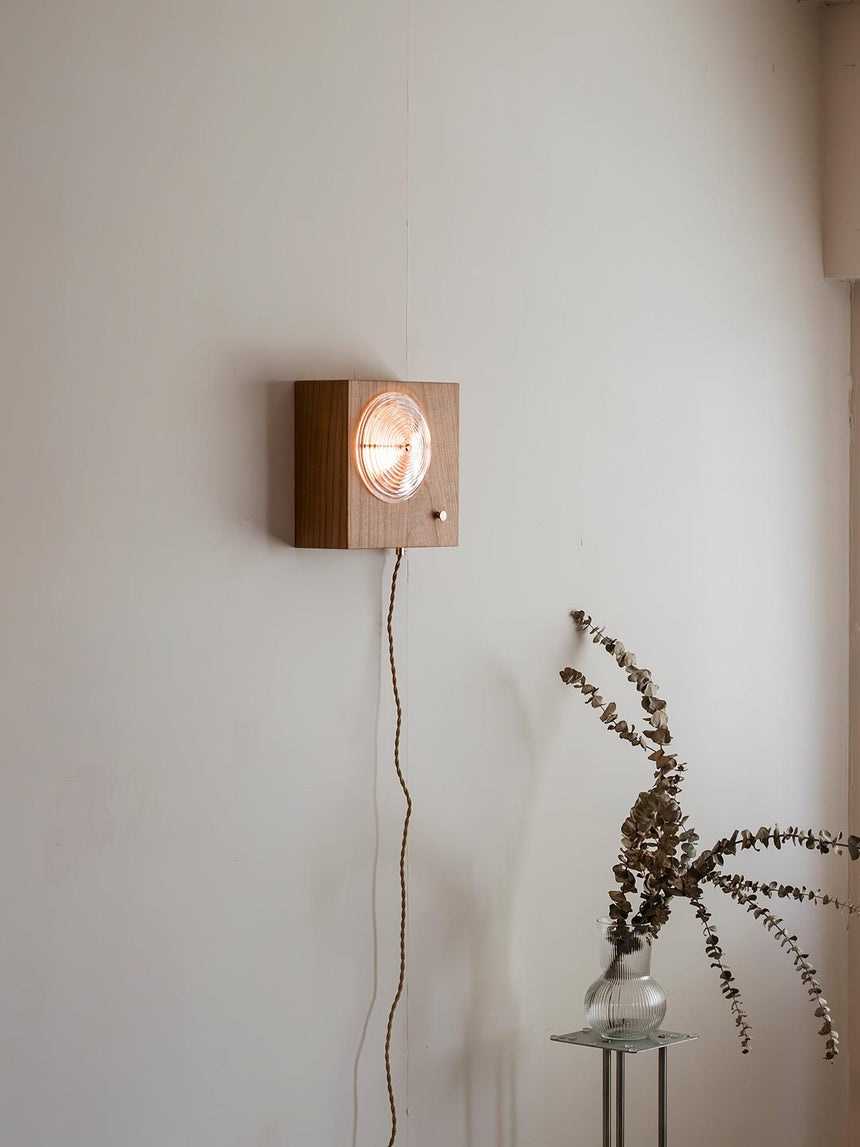 Wood box sconce lit on a wall above a small table with dried branches
