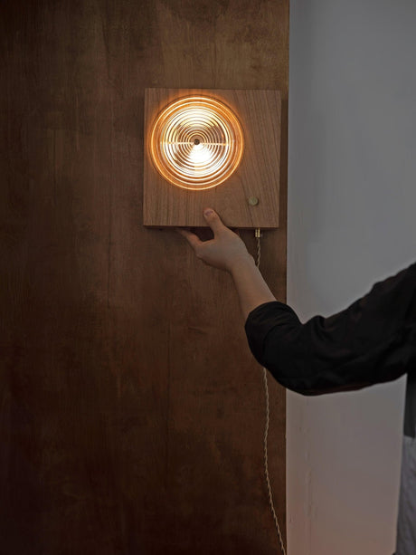 A hand placing the wood box against a dark wall during mounting