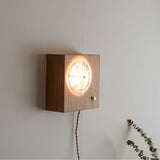 Wood box sconce lit on a white wall with dried stems beside it