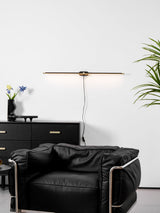 Gold rod lit above a black cabinet and a leather armchair, cord hanging down