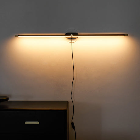 Rod lit on a dark wall above a black chest of drawers at night