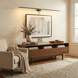 Slim rod lit above a framed print over a long walnut console with books and a vase
