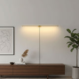 Slim gold rod lit on a pale wall between a framed print and a tall plant