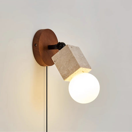 Sconce lit on a pale room wall, the cord running down under the walnut disc