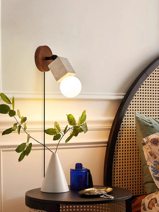 Sconce lit beside an arched cane mirror above a table with a plant and a vase