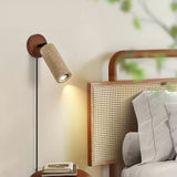 Sconce lit above a nightstand of books beside a cane headboard and cushions