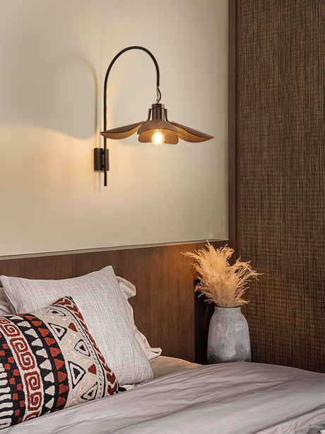 Sconce lit above a bed with a wood headboard and woven cushions