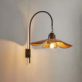 The petal shade lit on a pale wall, the arm curving out of its plate