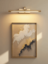 Gold bar lit over a framed abstract artwork on a warm painted wall