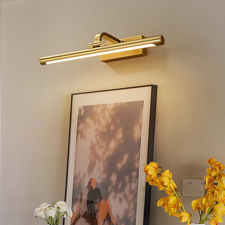 Gold bar lit over a framed print resting beside flowers on a console