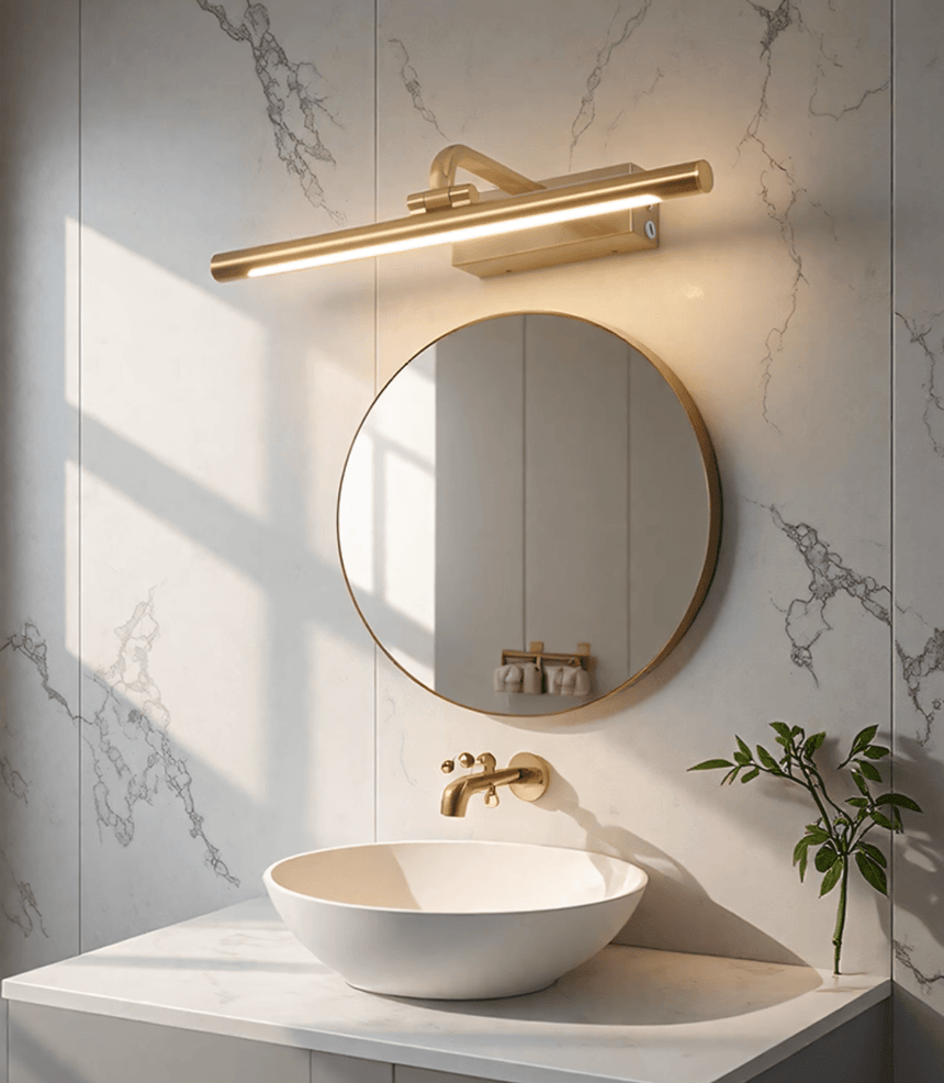 Gold bar lit above a round mirror on marble, over a stone basin and a plant