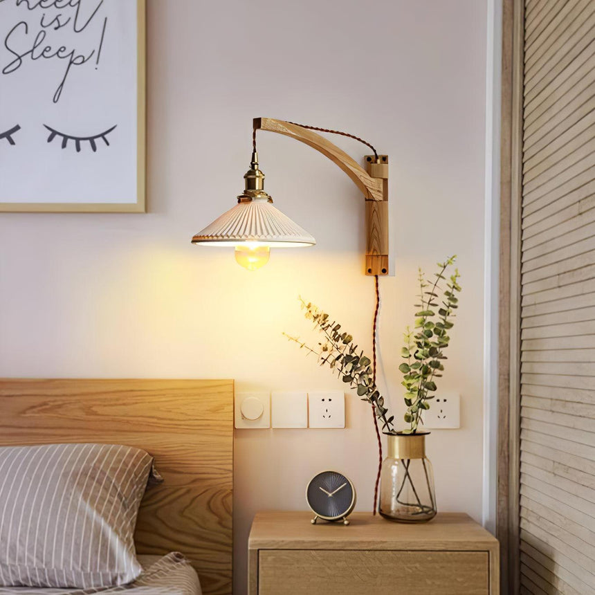 The lamp lit above a wood nightstand with a clock and a vase beside a bed