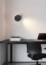 Lit above a dark desk and office chair, the beam grazing the wall downward