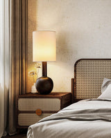 Walnut table lamp lit on a nightstand beside a cane bed