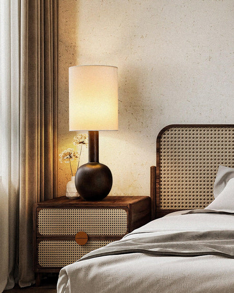 Walnut table lamp lit on a nightstand beside a cane bed