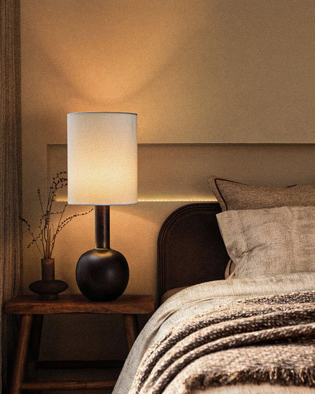 The black version lit on a nightstand beside a made bed
