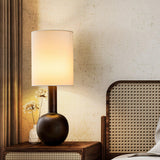 The black version lit on a console beside a cane headboard