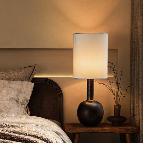 Walnut table lamp lit on a nightstand beside a made bed