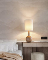 Walnut table lamp lit on a pale nightstand against a plaster wall