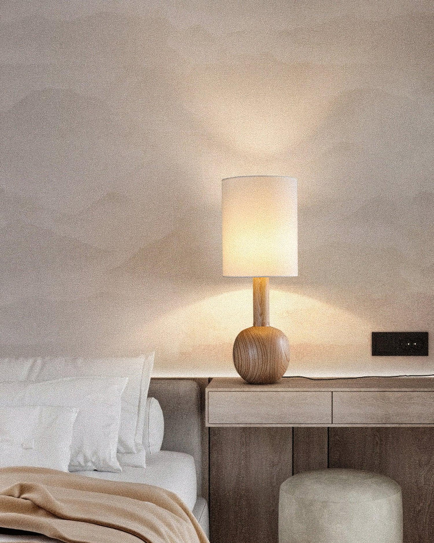 Walnut table lamp lit on a pale nightstand against a plaster wall