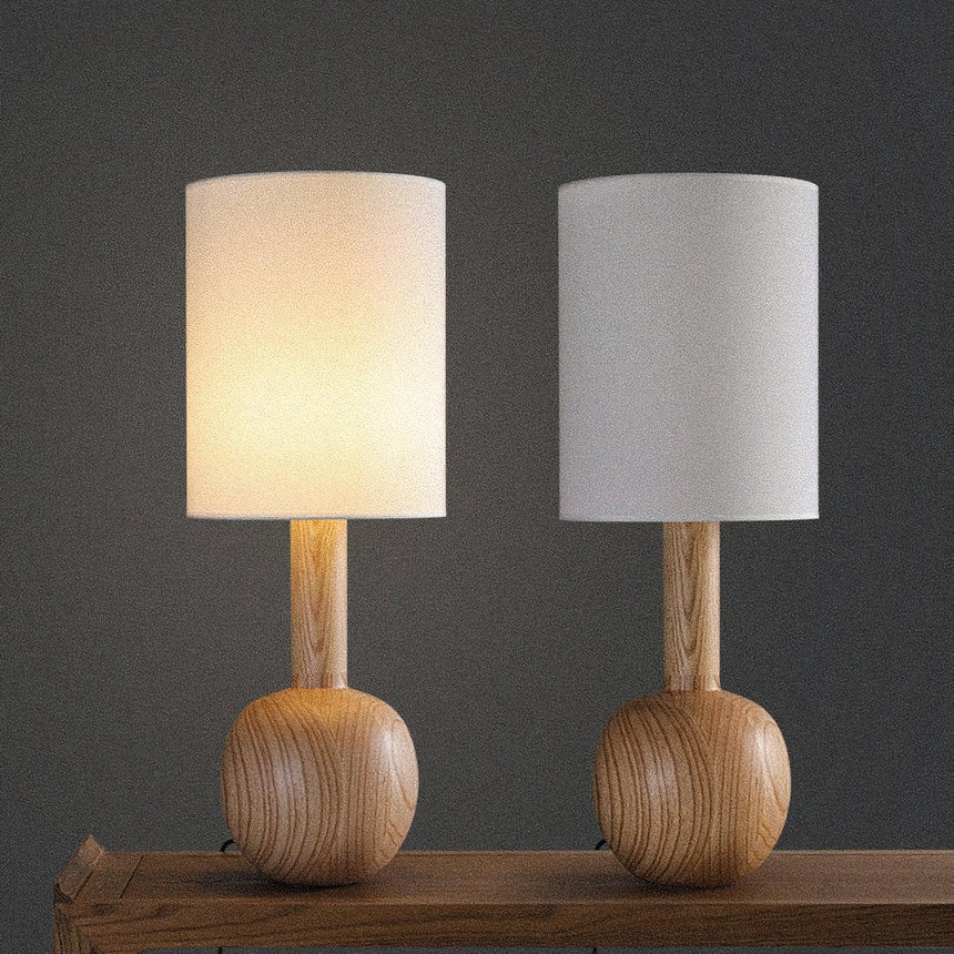 Two walnut table lamps on a wood table against a dark ground