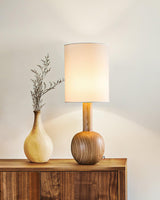 Walnut table lamp lit on a sideboard beside a pale ceramic vase