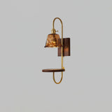 Amber glass shade lit above a walnut shelf and a brass loop frame