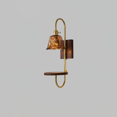 Amber glass shade lit above a walnut shelf and a brass loop frame
