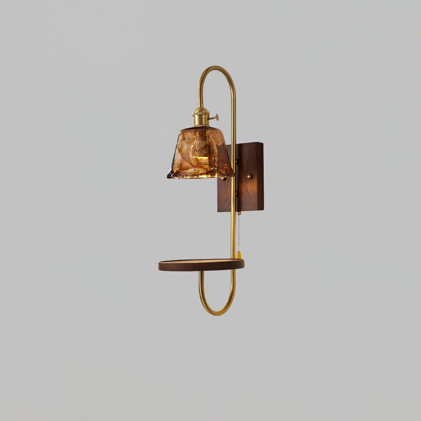 Amber glass shade lit above a walnut shelf and a brass loop frame