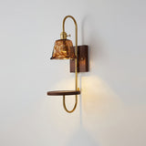 Amber shade lit warm, the walnut shelf and brass loop below it