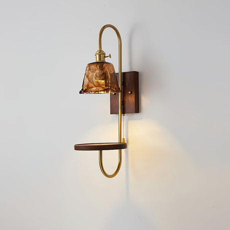 Amber shade lit warm, the walnut shelf and brass loop below it