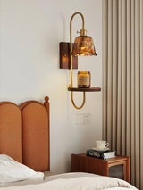 Sconce lit beside a bed, a cup and a book below the lit shade